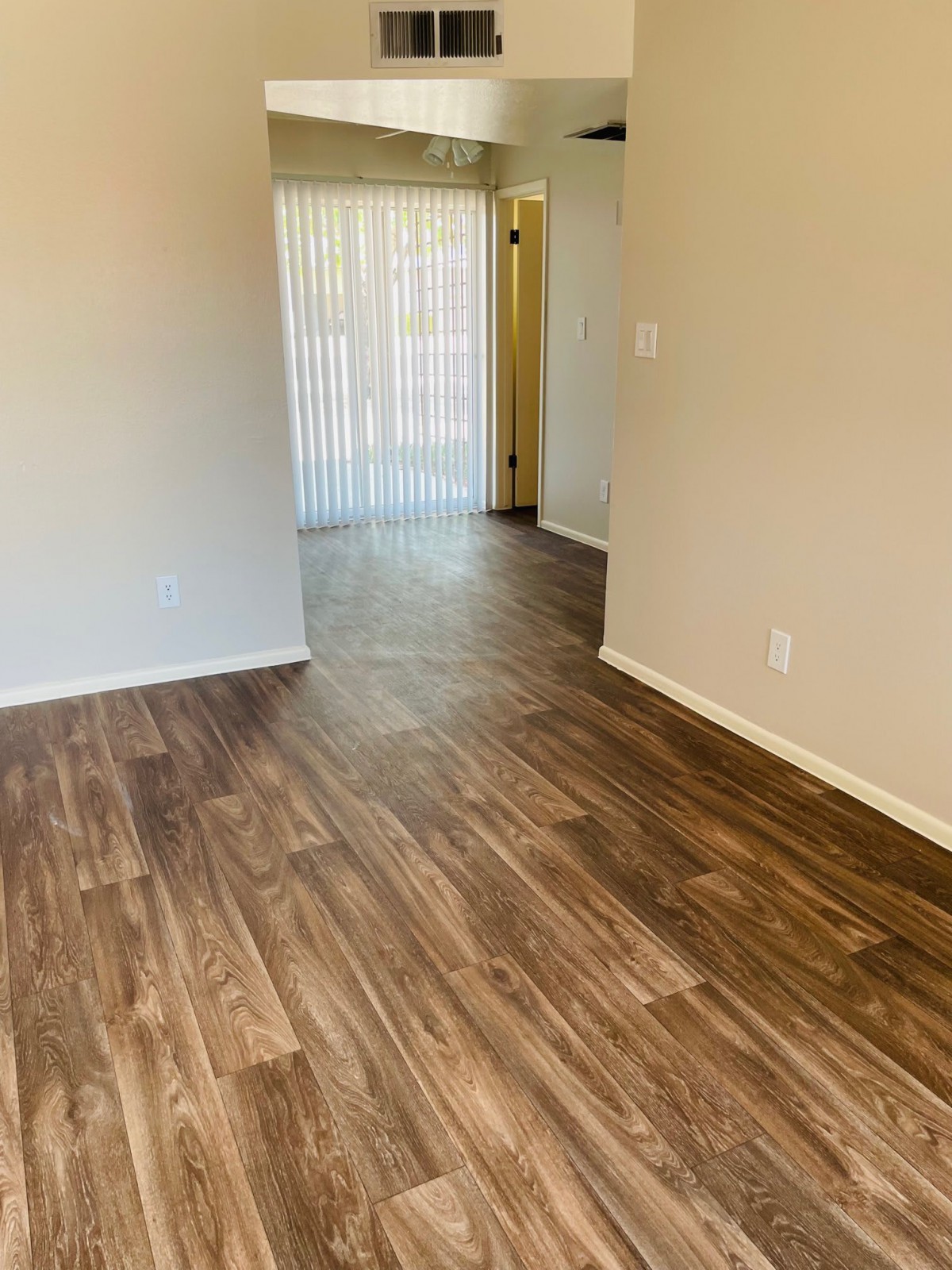 An empty living room with wooden flooring and a doorway leading to another area.