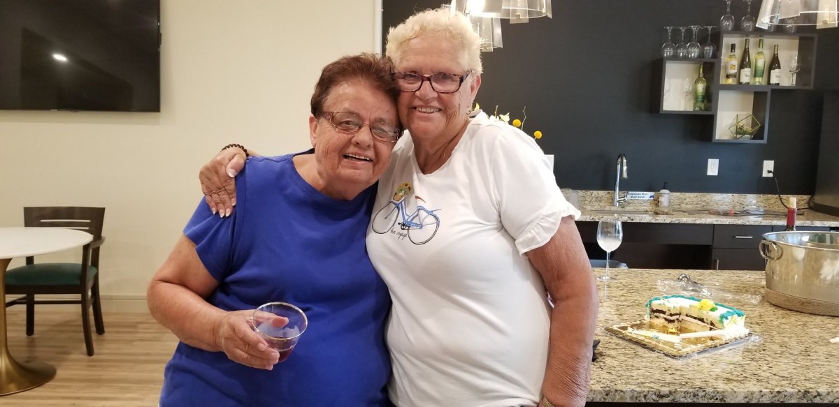 Two senior friends embracing and smiling indoors at a celebration.
