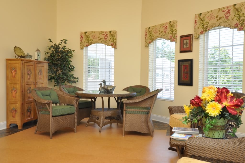 A cozy living room with wicker furniture and large windows, featuring warm decor and indoor plants.