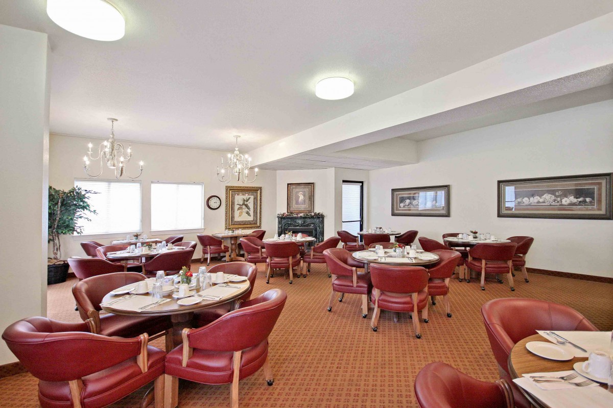 A spacious dining area featuring red leather chairs, round tables, and elegant chandeliers.