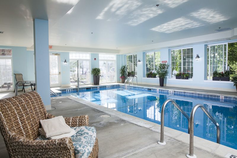 A luxurious indoor swimming pool area with ample natural light and comfortable seating.