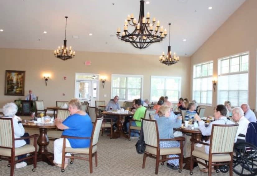 A group of people dining in a well-lit room with chandeliers.