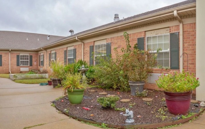 A brick house with a well-maintained garden and patio area under a cloudy sky.