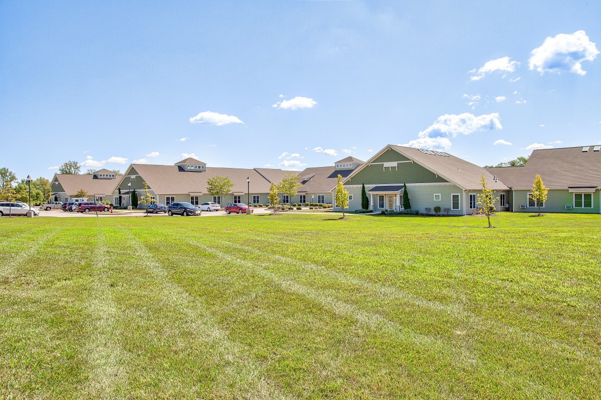 A wide view of a residential building surrounded by a large green lawn and under a clear blue sky.