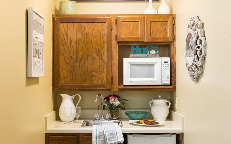 A small kitchen area with a microwave, wooden cabinets, a sink, and various kitchen items on the countertop.