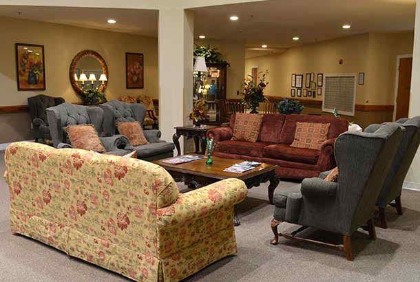 A cozy living room with a variety of sofas and armchairs arranged around wooden coffee tables, featuring warm lighting and decorative elements.