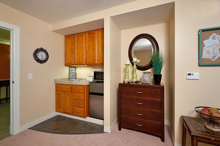 A cozy kitchenette area with wooden cabinets next to a dresser adorned with a decorative mirror and ornaments.
