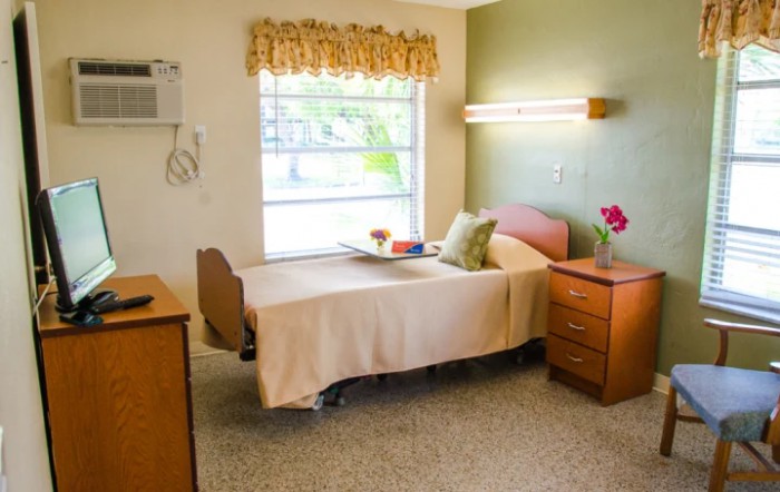 A hospital room featuring a single bed, nightstand, and window with floral curtains.