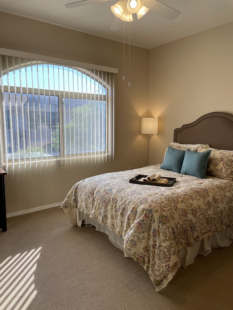 A cozy bedroom featuring a bed with patterned bedding, pillows, and abundant natural light through a large window.