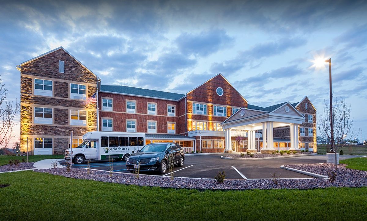 A modern hotel building with a parking lot and vehicles in the evening light.