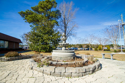 A beautifully crafted fountain surrounded by greenery and a clear blue sky.