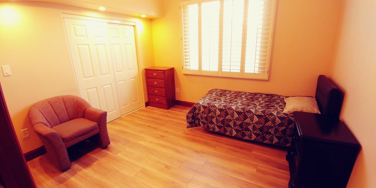 A cozy bedroom with wooden flooring, featuring a single bed, a dresser, and a window with shutters.