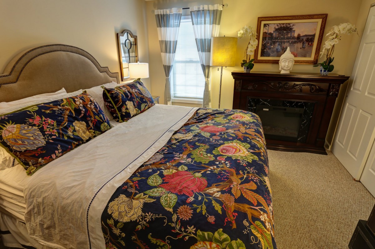 A cozy bedroom with a floral-patterned bedspread and pillows, featuring warm lighting and elegant decor.