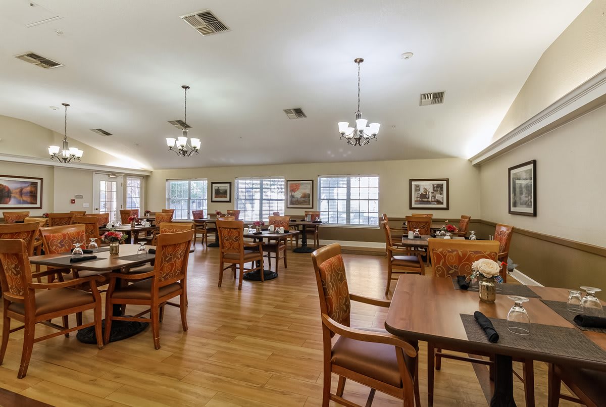 A spacious dining room with wooden tables and chairs, illuminated by chandeliers.