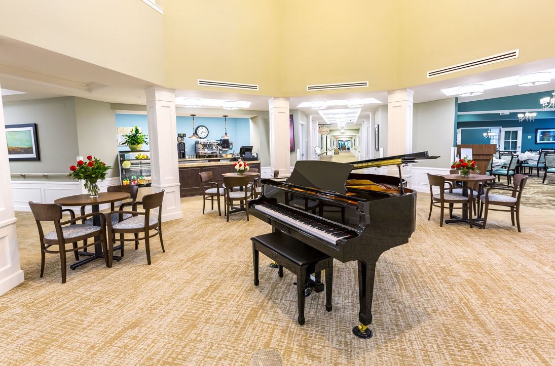 A spacious lobby featuring a grand piano surrounded by tables and chairs, with stylish decor and lighting.