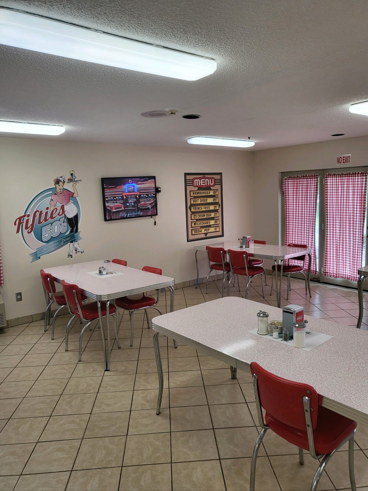 A retro-style diner with red chairs, white tables, and nostalgic wall art.