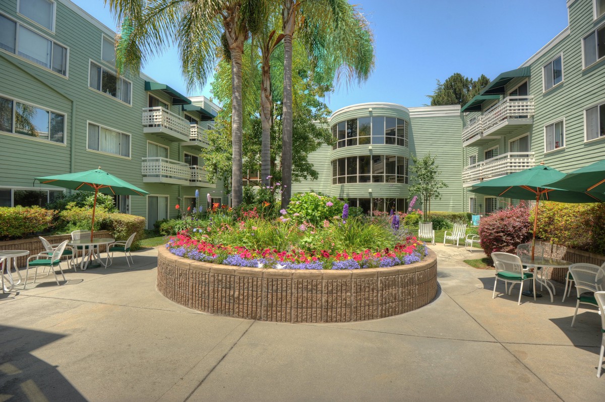 A vibrant courtyard with a flower garden surrounded by apartment buildings under a clear blue sky.
