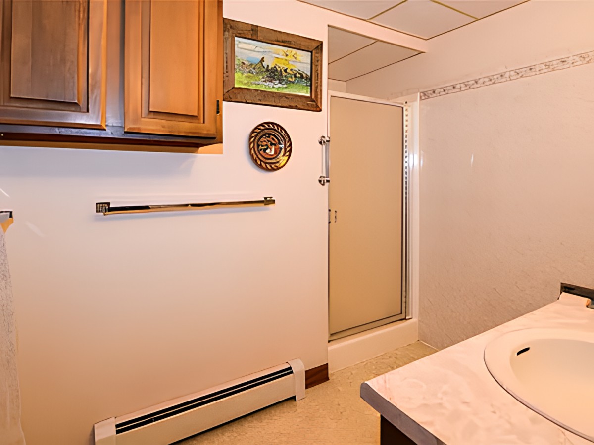 A bathroom with a wooden cabinet, shower, and wall decorations.