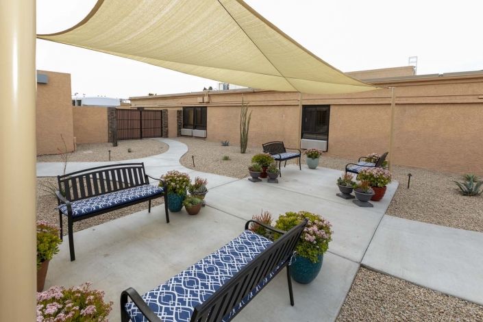 A cozy patio area with benches, shade sails, and potted plants in a desert landscape.