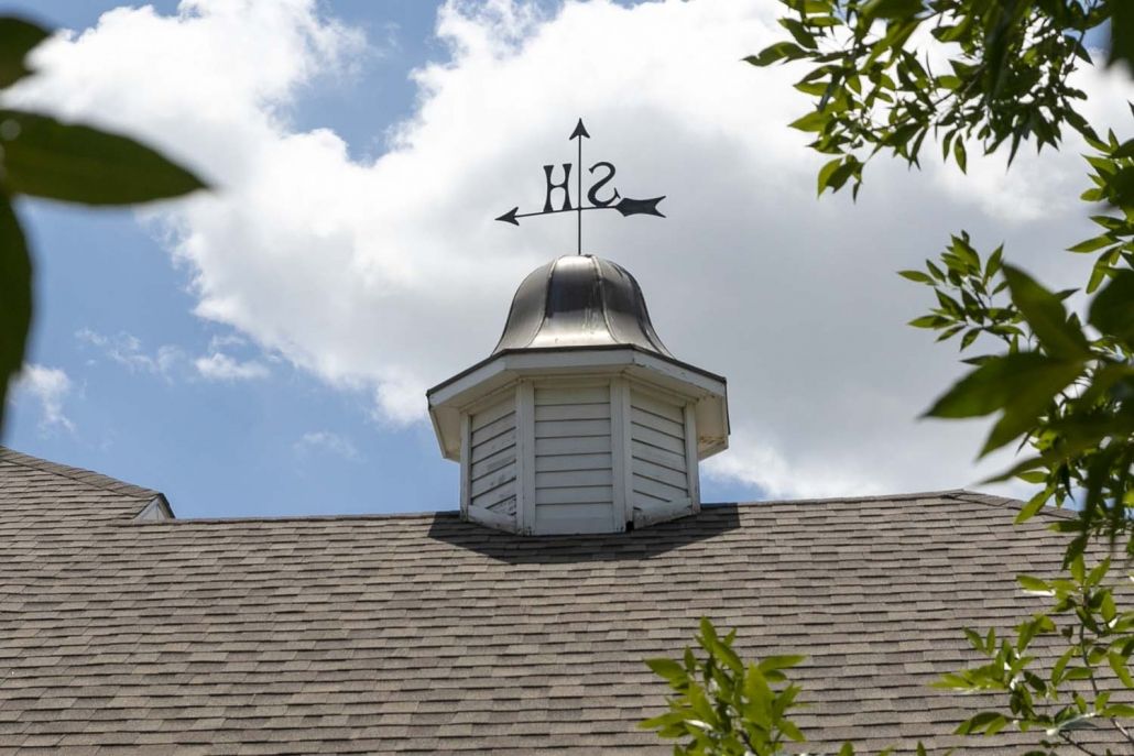 A rooftop cupola with a weathervane pointing directions against a cloudy sky.