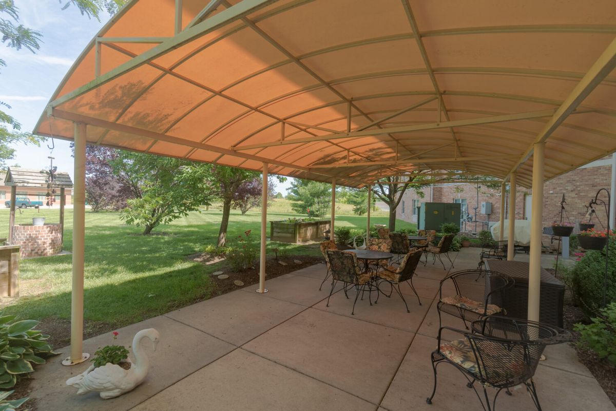 A cozy patio with an awning providing shade over tables and chairs, overlooking a lush garden.