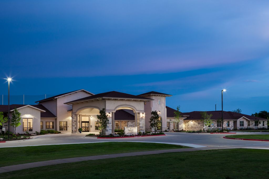A well-lit building with an arched entrance at dusk, surrounded by open green space.
