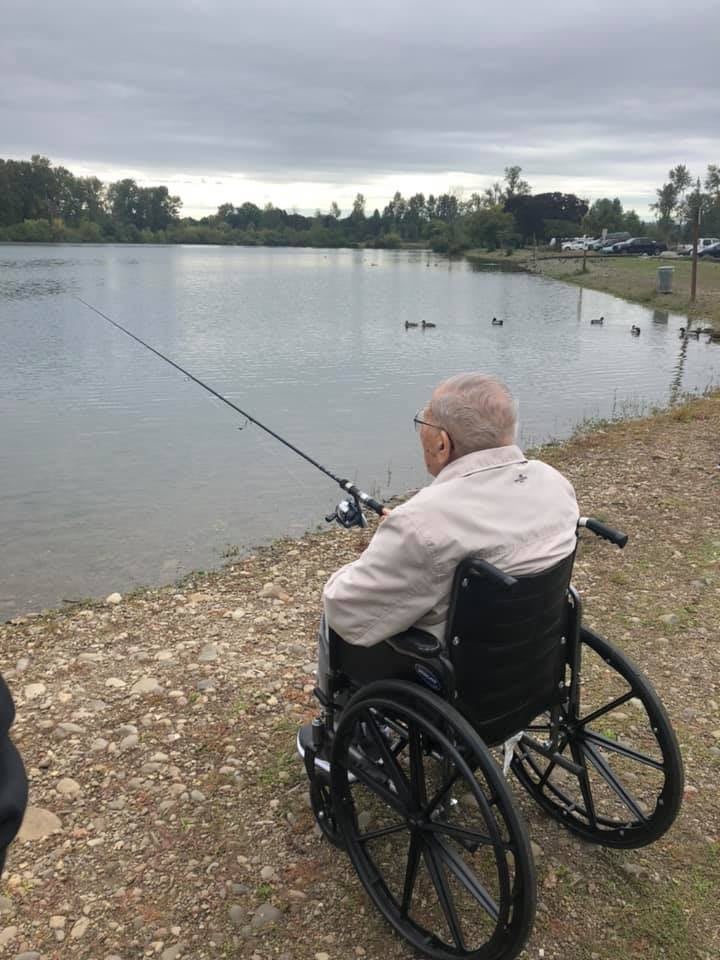 A senior person in a wheelchair fishing by a lake.