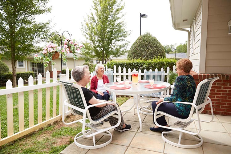A group of seniors enjoying a conversation on a patio surrounded by a garden.