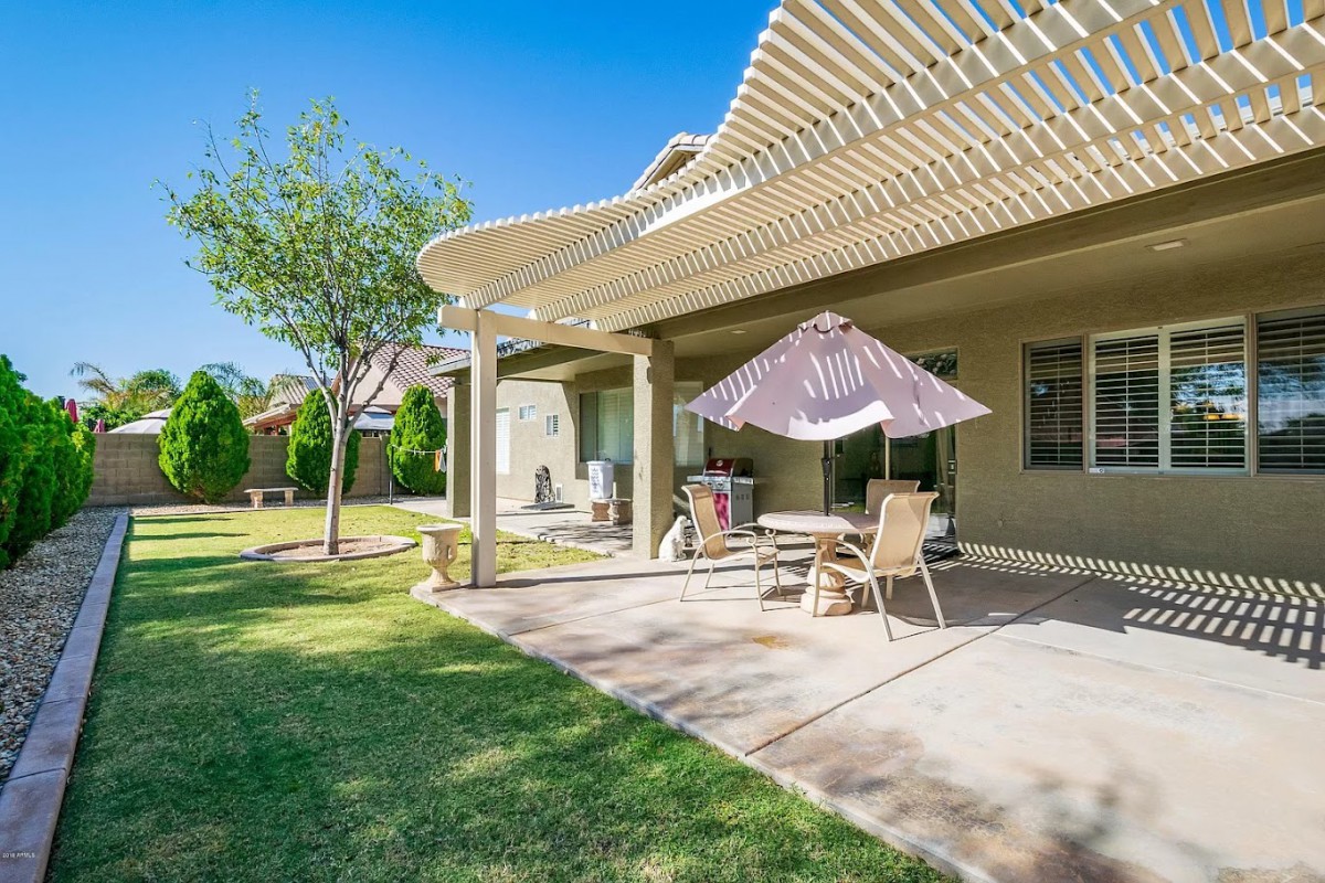 A sunny backyard patio with outdoor furniture and a pergola.