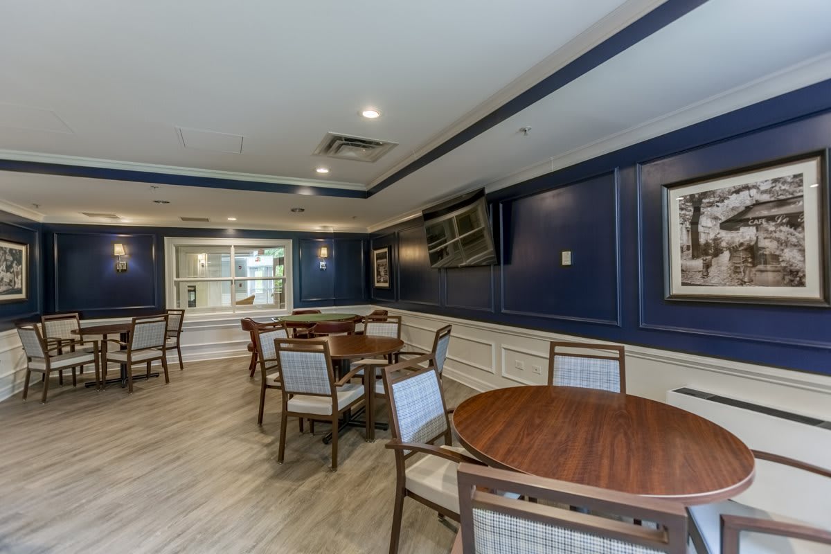 A spacious and elegant dining area with blue walls, featuring multiple tables and chairs, a TV mounted on the wall, and wood flooring.
