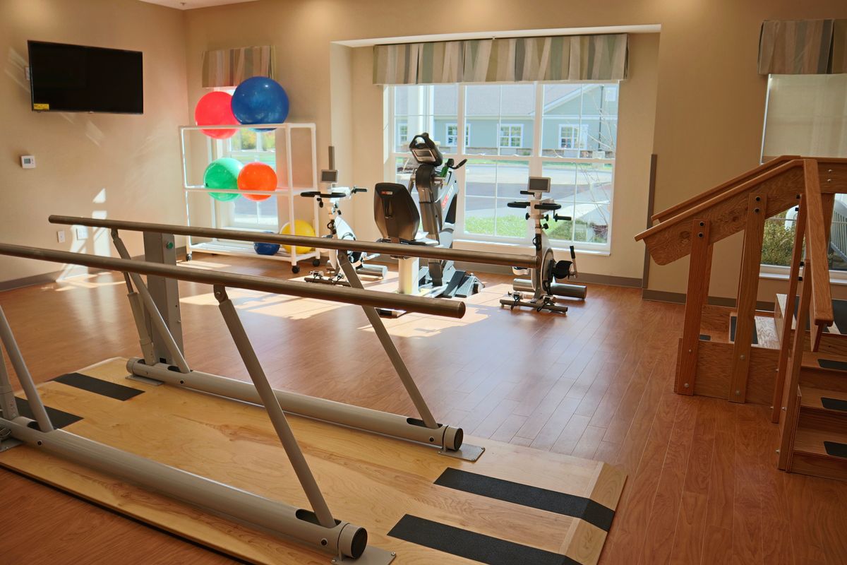 A well-equipped physical therapy room featuring parallel bars, gym balls, and various exercise machines.