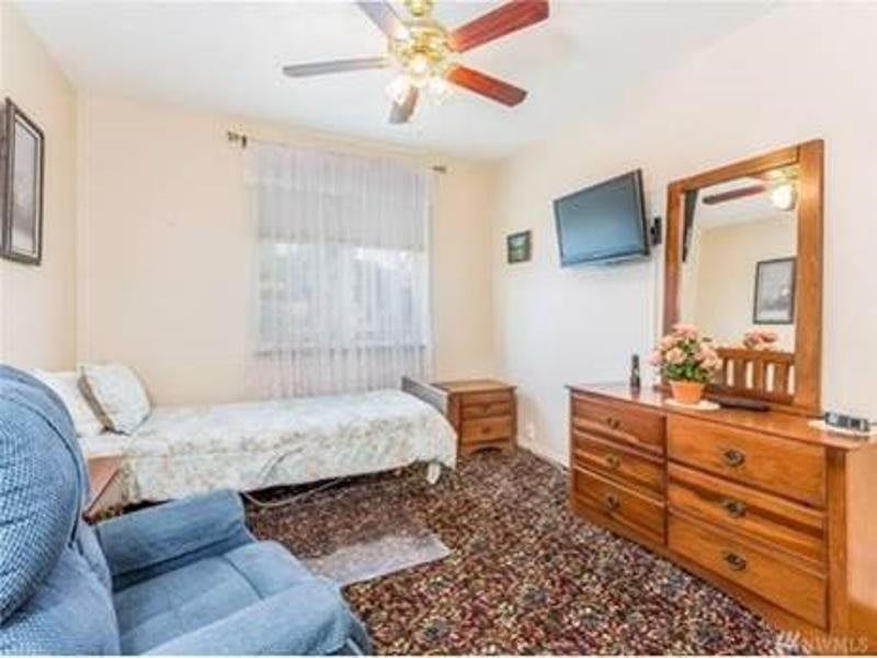A cozy bedroom with a single bed, dresser, wall-mounted TV, and a ceiling fan.