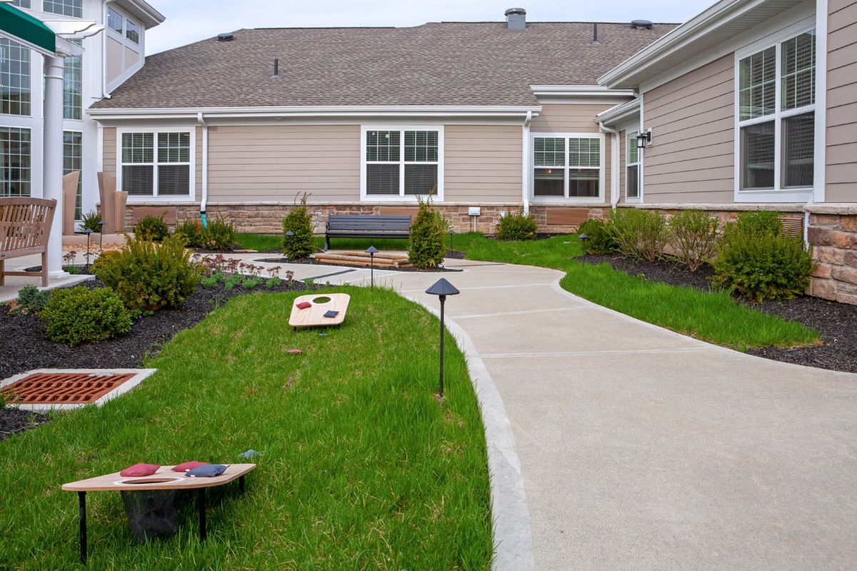A residential backyard with a cornhole game set up on the lawn alongside a concrete pathway.