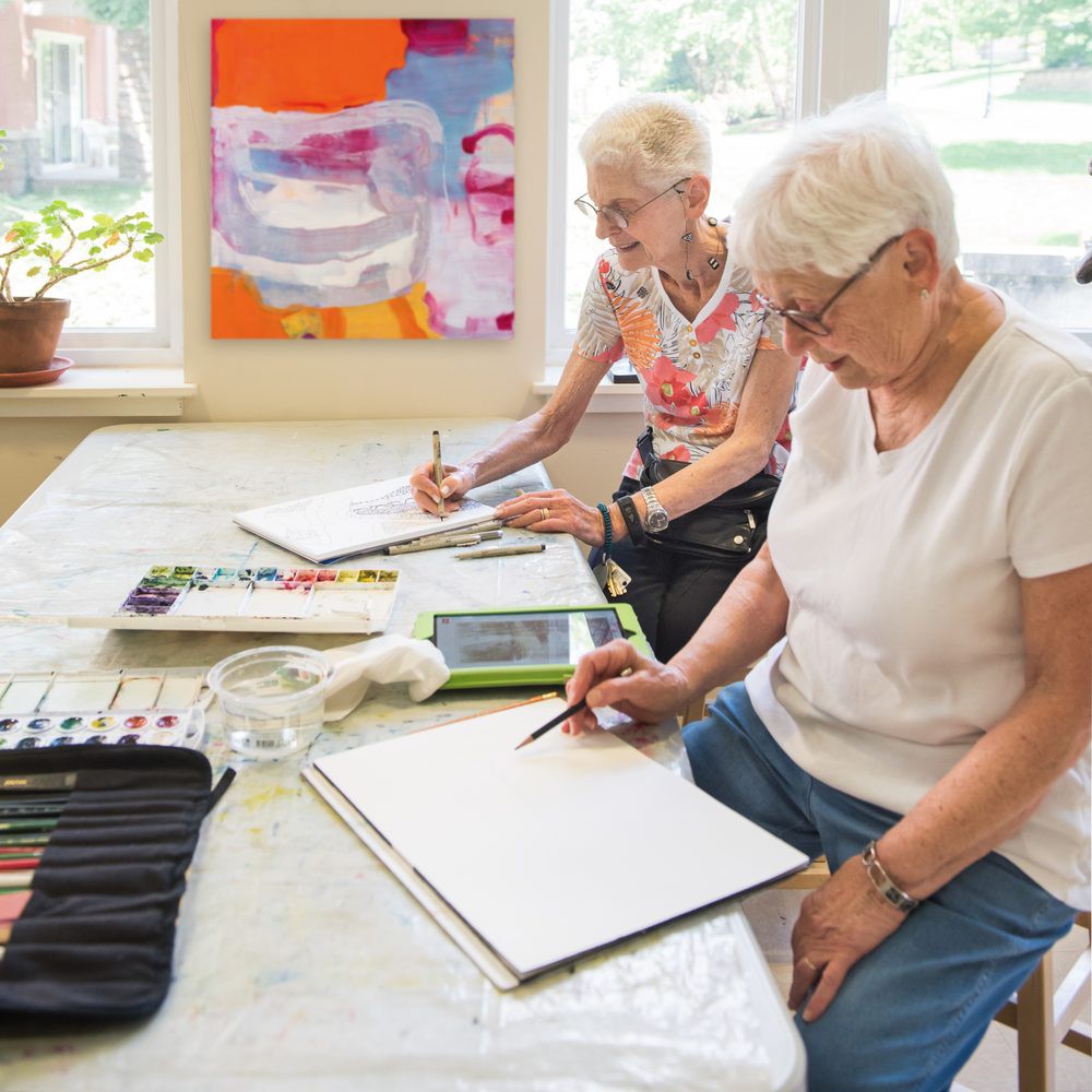 Two seniors engaged in a painting session, focusing on their artwork.