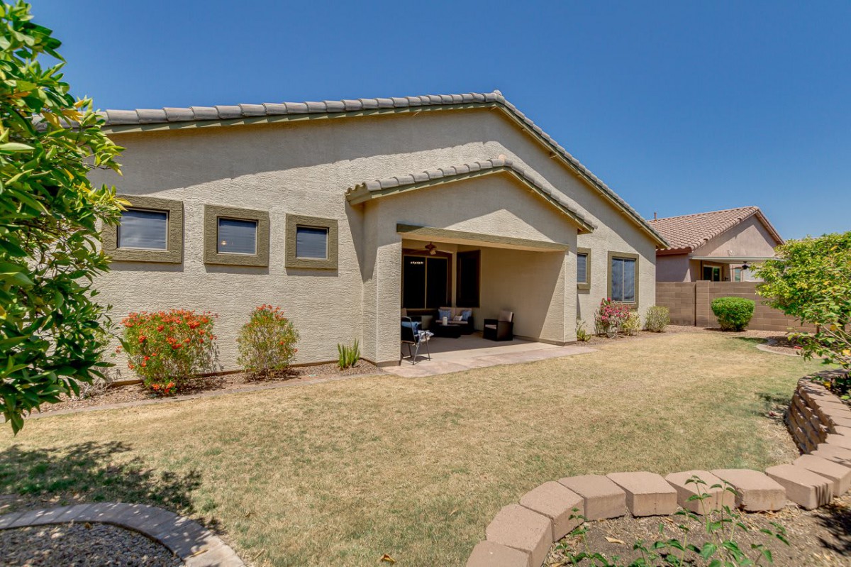 A suburban house with a grassy backyard and covered patio under a clear blue sky.