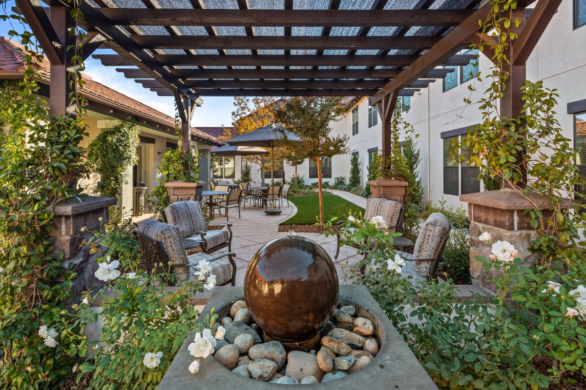 A beautifully landscaped outdoor garden with a fountain and seating area under a pergola.