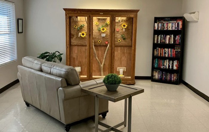 A cozy lounge area featuring a leather couch, a wooden cabinet with sunflowers, and a bookshelf filled with books.