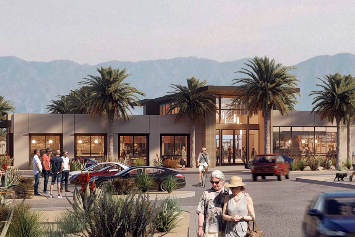 A modern shopping center surrounded by palm trees, with people walking and cars parked in front of the building, set against a backdrop of mountains.