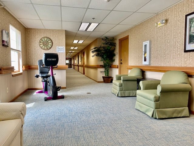 A hallway featuring exercise equipment, two chairs, a plant, and a clock on the wall.