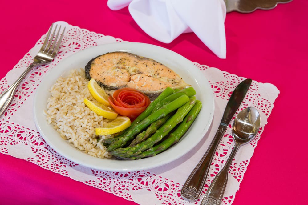 A plate of salmon served with rice, asparagus, and lemon slices on a neatly arranged table setting.