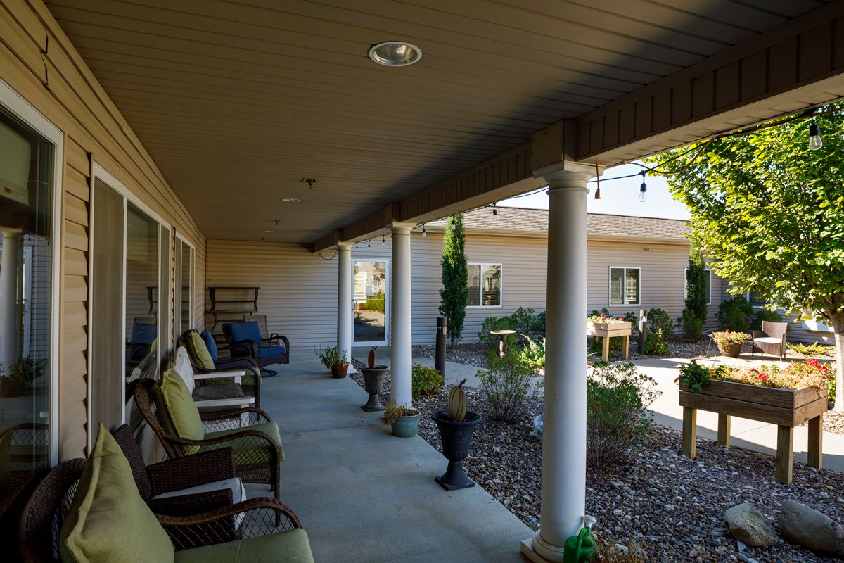 A covered porch with seating and landscaping, featuring columns and a garden area.