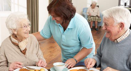 A caregiver assists elderly residents during a meal in an assisted living facility.