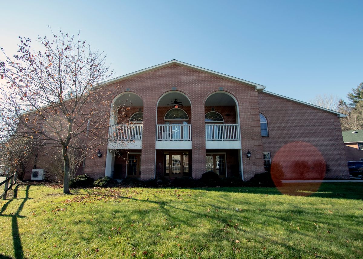 A two-story brick house with arches and balconies, surrounded by a grassy lawn.