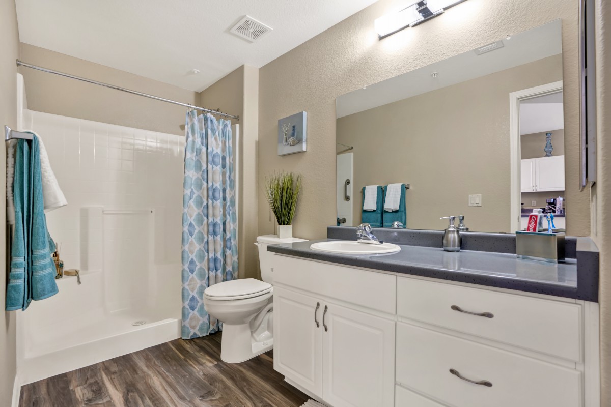 A modern bathroom featuring a sink with a large mirror, a shower with a blue curtain, and neatly arranged towels.