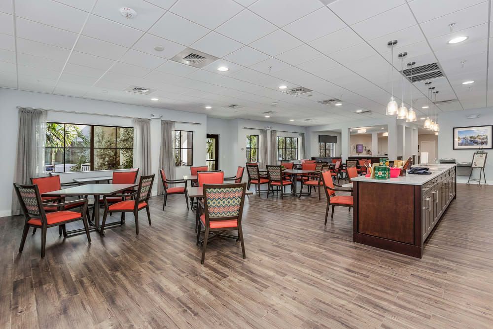 A modern dining area with wooden floors and red-cushioned chairs around multiple tables.