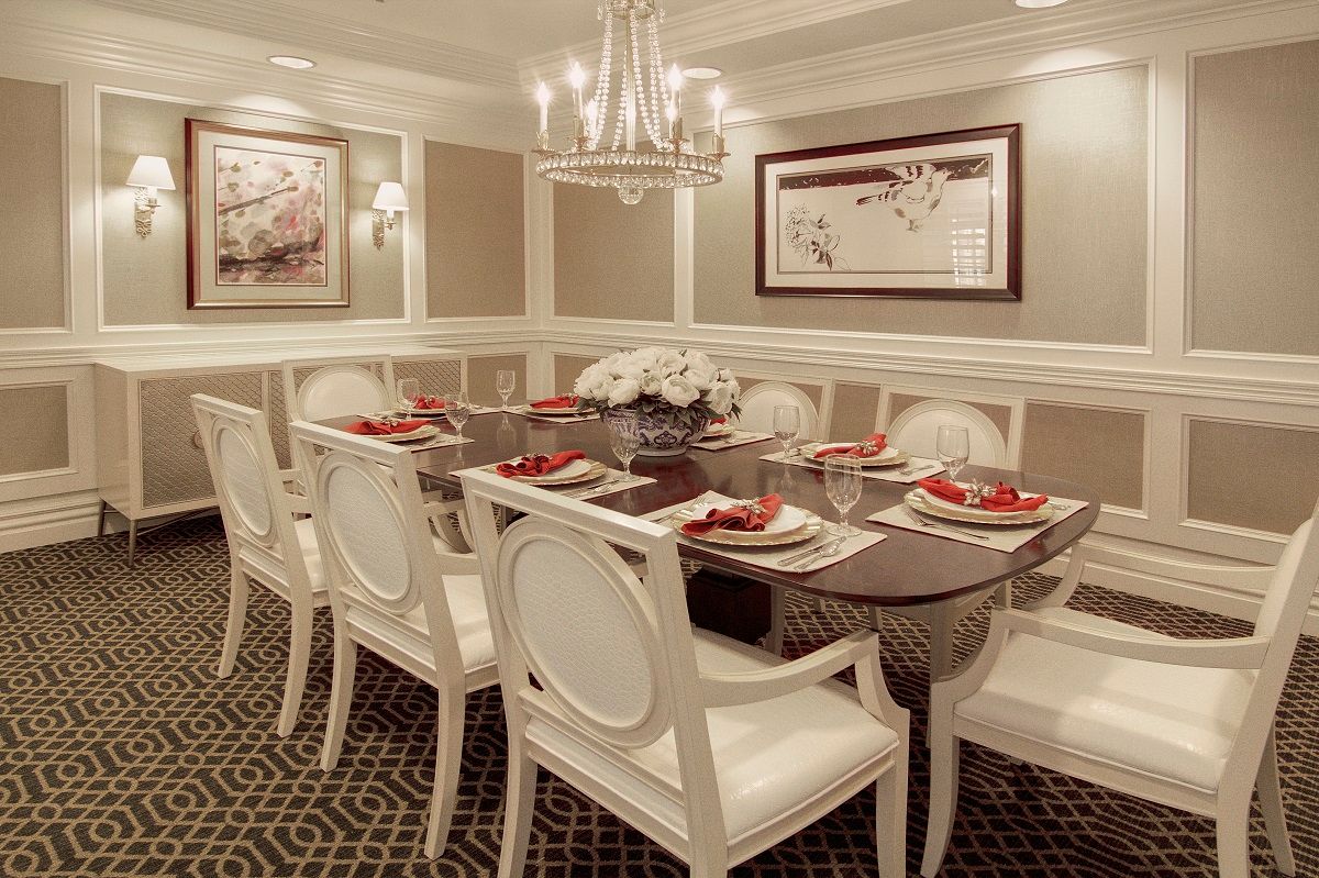 A luxurious dining room with an elegant chandelier, featuring a sophisticated table setting and white upholstered chairs.
