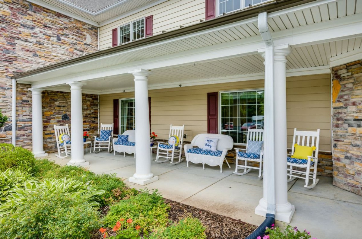 A cozy porch with rocking chairs and columns, overlooking a landscaped garden.
