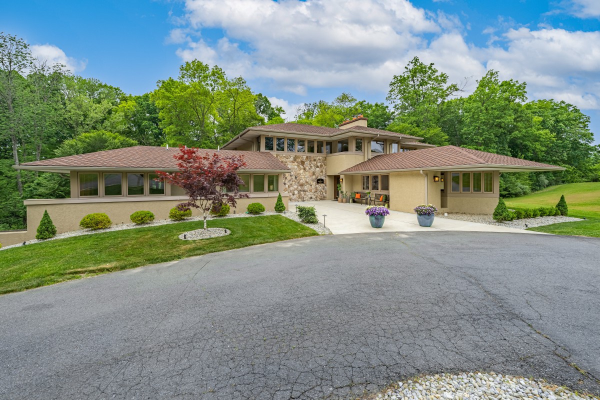 A modern house with a spacious driveway and landscaped gardens surrounded by trees under a blue sky.