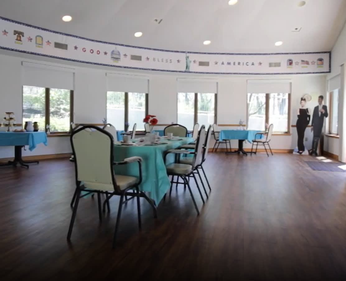 A bright event hall set up with tables and chairs, decorated with blue tablecloths.