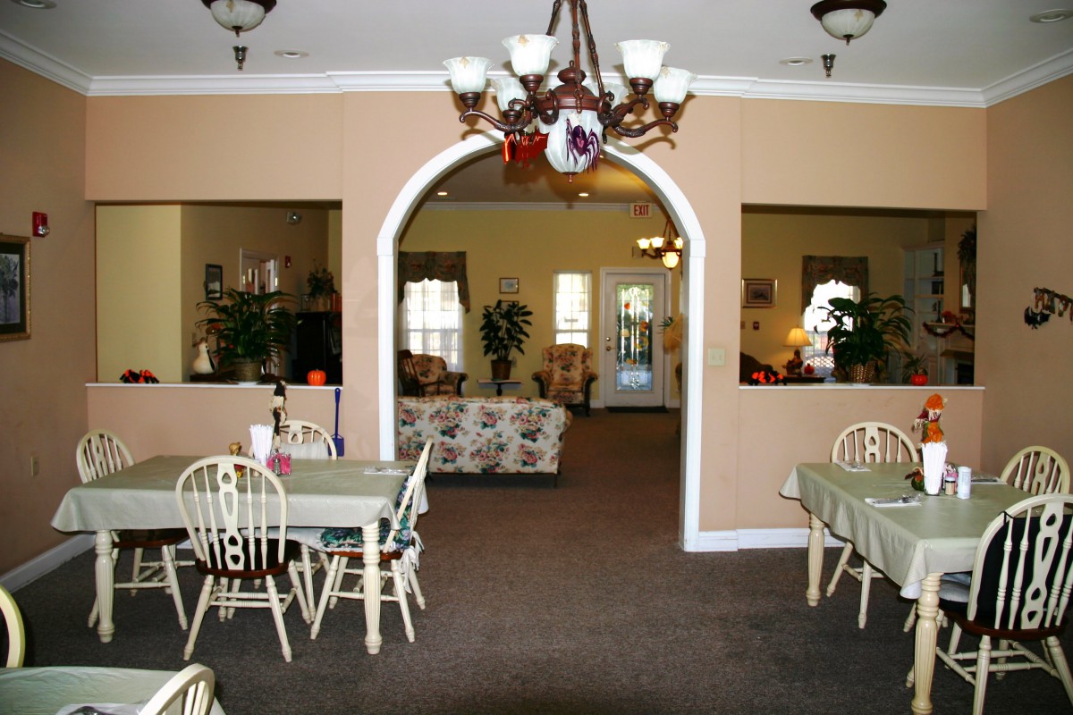 A cozy interior with a dining and living area separated by an archway, featuring elegant chandeliers and classic furniture.